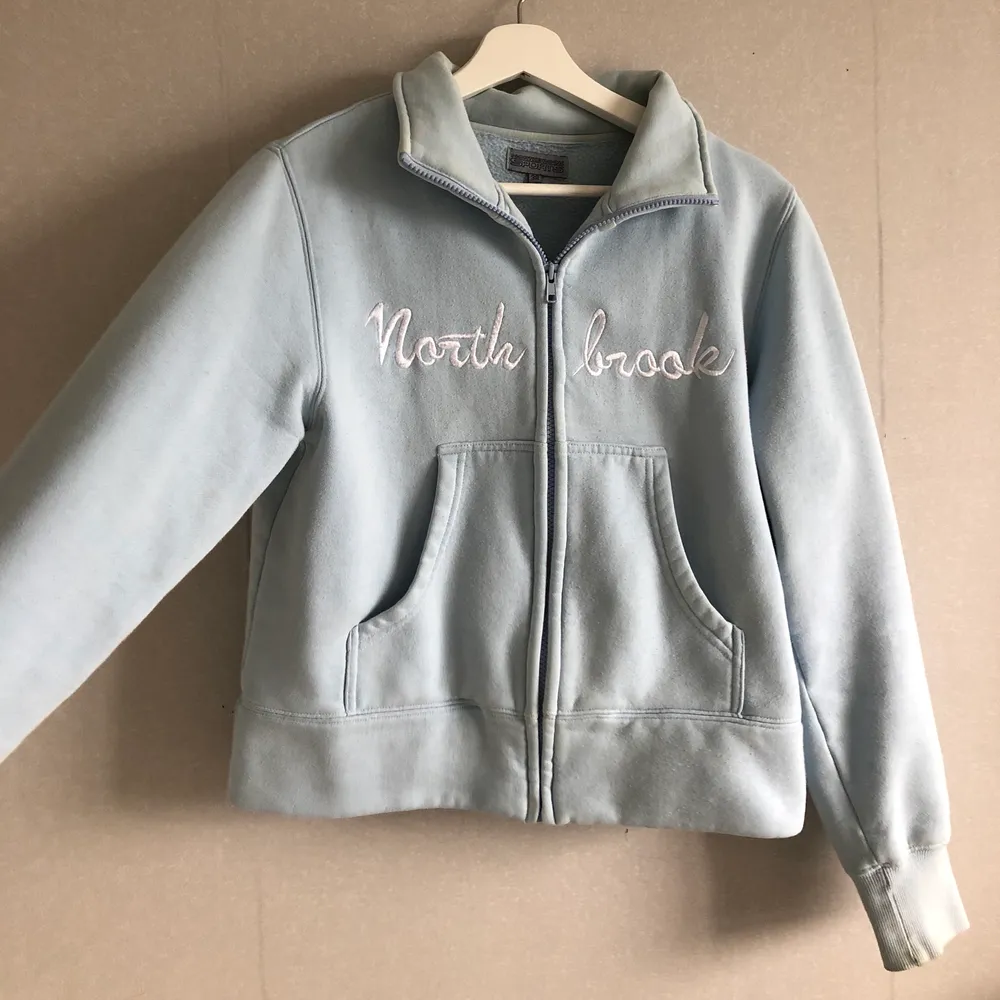 Ljusblå sweatshirt med dragkedja, broderad text ”North brook”. Tyvärr lite nopprig då den är ganska gammal💕Kan mötas upp i stockholm/köpare står för frakt❤️ . Tröjor & Koftor.