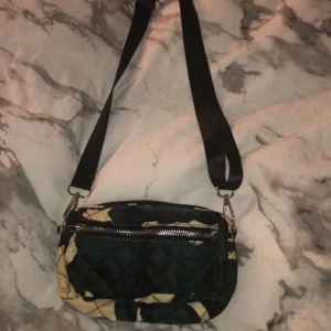 Liten väska - Liten väska med camoflauge mönster. Ett stort fack och ett lite mindre fram. Går att använda både som bumbag och handväska. Använd fåtal gånger! Köpare står för frakt, står ej för postens slarv. Katt finns i hemmet, om du undrar något mer, tveka inte att höra av dig 🥰