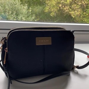 Svart väska från River Island - En svart väska med gulddetaljer från River Island. Axelbandet är reglerbart. Tre stycken fick, två större och ett lite mindre. Det finns dessutom fickor i väskan😇😇💕 frakt tillkommer!