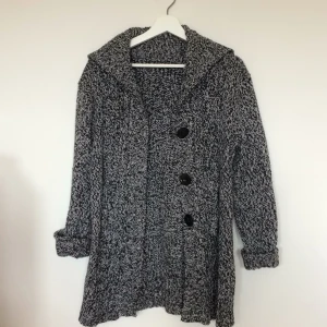  - Tjock, stickad kofta med stora knappar. Tillhörande bälte medföljer.