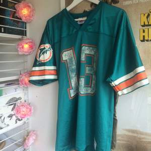 En oldschool, oversized team shirt för Miami Dolphins i något glansigt, sportigt material. Köpt på Beyond Retro. 