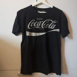 Svart T-shirt med Coca-Cola tryck i storlek M. Frakten ligger på 44 kr. 