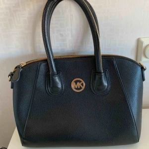 MK elegant rymlig väska i svart och guld!  - Fin väska i svart med gulddetaljer. MK, fått den i present, kan ej garantera äkthet. Ser exklusiv och dyr ut. Mellantor modell, rymmer mycket. Elegant och stilren modell. Skickas eller hämtas i centrala Göteborg.