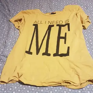 Det är en gul t-shirt med en liten text där det står ALL I NEED I ME. Köparen betalar frakt.