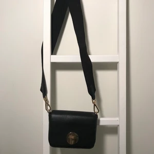 Väska från hm - Svart väska från hm med guld detaljer och ett tjockare strap. Perfekt längd för att ha som crossbody. Kommer egentligen med ett tunnare band men jag klippte av det och satte på ett tjockare. Köparen står för frakt. 