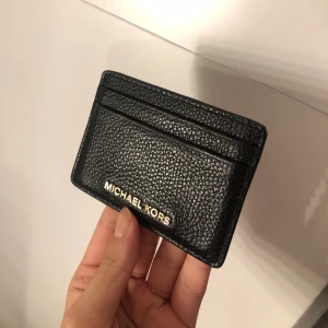 Äkta korthållare från michael kors - En svart korthållare köpt från MK med gulddetalj, äkta. Köpt från MK butiken i mall. Välanvänd dock fortfarande helt felfri. Totalt fem stycken kortfack. Men det går att pressa in flera kort om det önskas. 