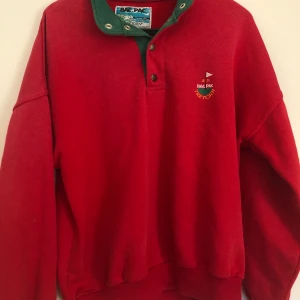 Röd sweatshirt  - Röd sweatshirt, tröjan har en grön krage men om man knäpper alla knapparna så syns inte kragen. Köpt på secondhand men använd ett fåtal gånger av mig. Tröjan har en liten fläck på höger arm (syns på sista bilden), men det är inte något man tänker på. 