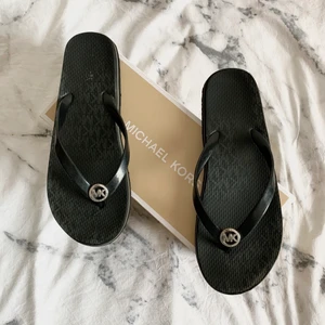Michael Kors flipflops - Flipflops från Michael Kors, de är i fint skick men som ni kan se så har MK loggorna på ”sulan” suddats ut lite. Kommer i originalkartong 🌺