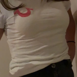 True religion T-shirt  - En vit T-shirt från true religion, använder den ej då jag inte gillar rosa, trycket på baksidan är lite förstört av tvätten men det ser lite coolt ut, köparen står för frakt 