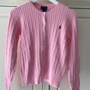 Helt oanvänd kabelstickad kofta från Ralph Lauren. Prislapp sitter kvar. Färg: carmel pink. Storlek: XL/TG (16) barnstorlek, men skulle säga också passar dam i XS.  Frakt tillkommer