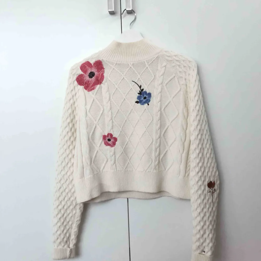 Säljer denna fina stickade tröja med hög krage från Tommy Hilfiger. Detaljer med broderade blommor i olika färger finns på framsidan samt ärmar. Använd ca tre gånger. . Stickat.