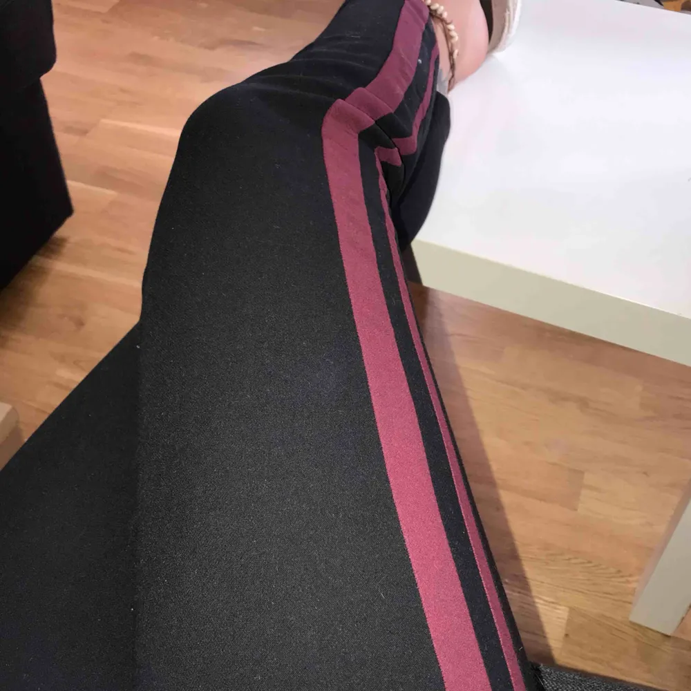 Kostymbyxor med detaljer på utsida ben, i form av två linjer i vinröd färg.  Byxorna är supersköna och nästintill helt oanvända, dom kommer ifrån Lindex Storlek; 38 . Jeans & Byxor.
