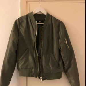  - Grön bomberjacka i fint skick med gulddragkedja på ena ärmen. Köparen står för frakten.
