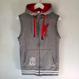  - Hoodie utan ärmar i grå melange, vitt och rött broderi, röda remmar och foder i luvan. Jättefin kvalitet, nyskick. Liverpool / L.F.C