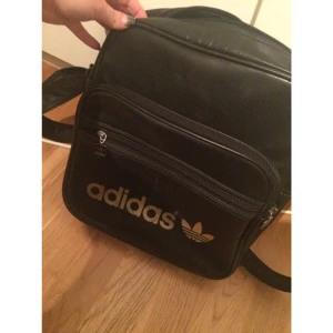  - Svart adidas väska med guld text. Lite sliten men håller fortfarande. Praktisk väska med många fack, men använder den inte längre.  OBS! Ska varan fraktas betalar köparen för den kostnaden 