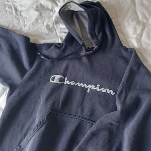 Champion hoodie - En vintage champion hoodie i mörkblå färg + grått märke och innertyg i huvan! Najs vintage fit när muddarna är lite insydda om ni förstår😅... står storlek M men passar najs oversize på mig som är en S. Liiite nopprig vilket syns på bild 2 men inget som förstör helheten. Ej säker på fraktkostnad ännu.