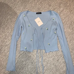 Ljusblå kofta och croptop! - Jättefint ljusblått set med både kofta och croptop 🦋 Helt oanvänt med lappen kvar. Tyget är räfflat med små vita broderade blommor. Den är köpt i storlek S men är flexibel och ganska stretchig. Köpt för 380kr men säljer för 280kr + frakt. Köparen står för frakten!💙 Säljer pga att jag inte har användning för dem. 