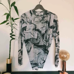  - En topp med marmortryck och omlott på framsidan. Tyg i polyester. Toppen kommer från Noir&Blanc och är i storlek XS. Frakt på 54kr tillkommer.