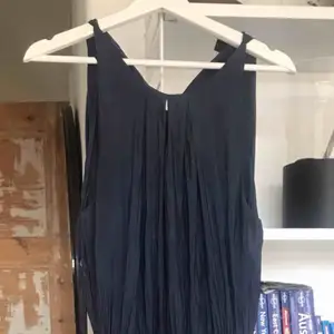 Marinblå plisserad långklänning. Använd en gång. Det är liten öppning framtill samt en öppning bak med knytdetalj. 