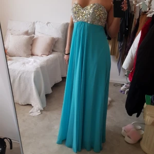  - Balklänning i turkos färg med glittriga stenar runt bysten. Jag är 170cm och den nuddar marken. Använd en gång och är i fint skick. Möts upp i Göteborg. Köparen står för frakten.