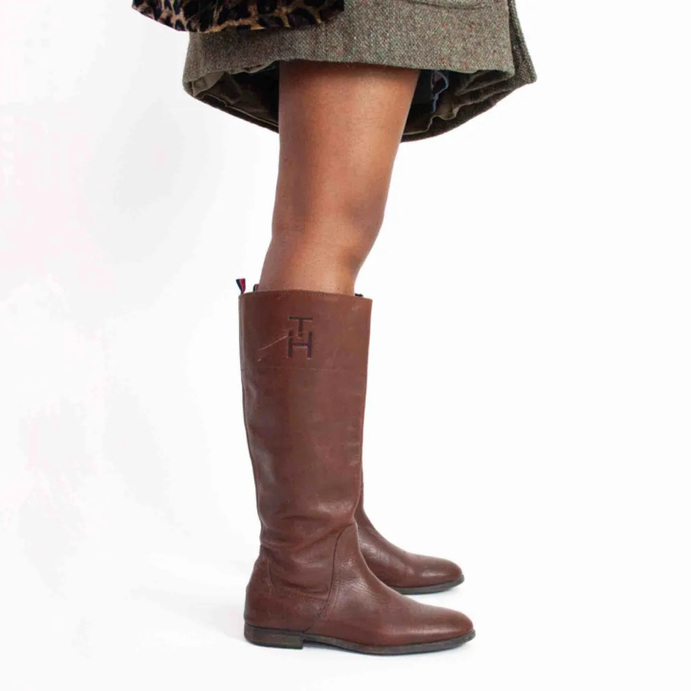Tommy Hilfiger knee high real leather boots in brown size 39 A visible scratch on the right shoe, no anti slippery protection SIZE Label: 39 EU, feels like true to size Model: 169/39 (shoes) Measurements: Foot: 27 cm Ankle: 29 cm Shin: 40 cm Height: 41 cm. Skor.