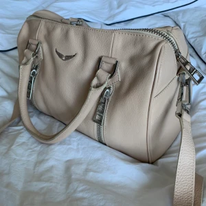 Zadig & Voltaire Sunny Medium Bag - Så fin Zadig väska i en beige/rosa färg. Perfekt storlek till skolan. Köpt sommaren 2019 och inte använd så mycket tyvärr. Jag köpte den i zadigs egen butik. Hittar inte  denna färgen på deras hemsida men finns i svart på Zalando.se och där kostar den 4 395kr. Skriv privat för fler bilder! Ni kan buda i kommentarerna också.