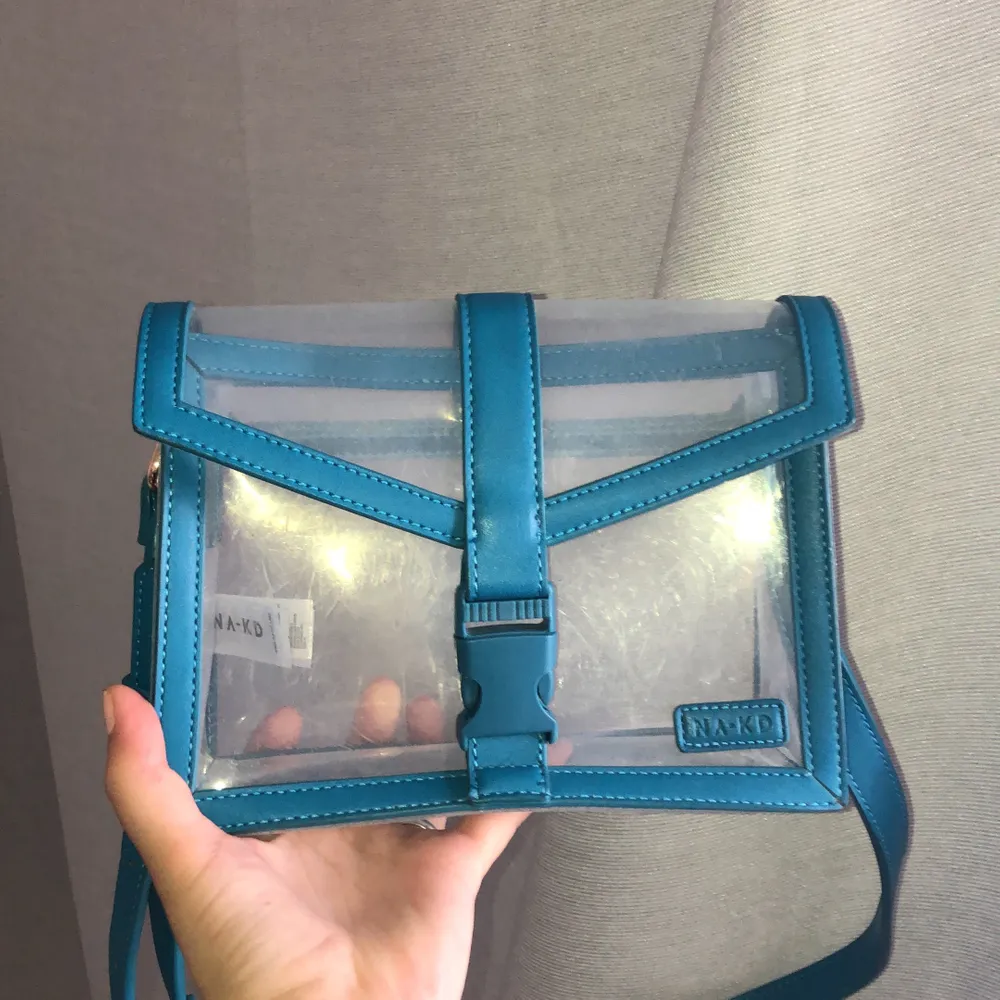 Assnygg blå transparent väska från nakd, justerbart axelband, kan bli väldigt lång och väldigt kort. Bra skick knappt använd. . Väskor.