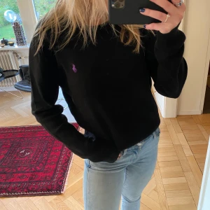 Ralph Lauren tröja - Säljer en så snygg tröja från Ralph Lauren, den är svart med ett lila märke, stl S men, så passar även M. (Invikt på bilden) Köpt för 1200kr💕