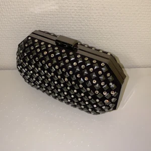 Liten clutch med strass - Gullig clutch i jättefint skick. Hård i ytterhöljet och alla nitar och strass sitter kvar, Använd men inte skadad. Axelkedjan går att vika in helt eller användas. 