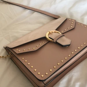 Axelbands Väska  - Väska med rosa och gulddetaljer. Eftersom det finns så många fack och två olika delar så rymms det väldigt mycket i den. Använd ungefär 5 gånger men annars är den som ny. Man kan också justera hur lång man vill att den ska vara. 