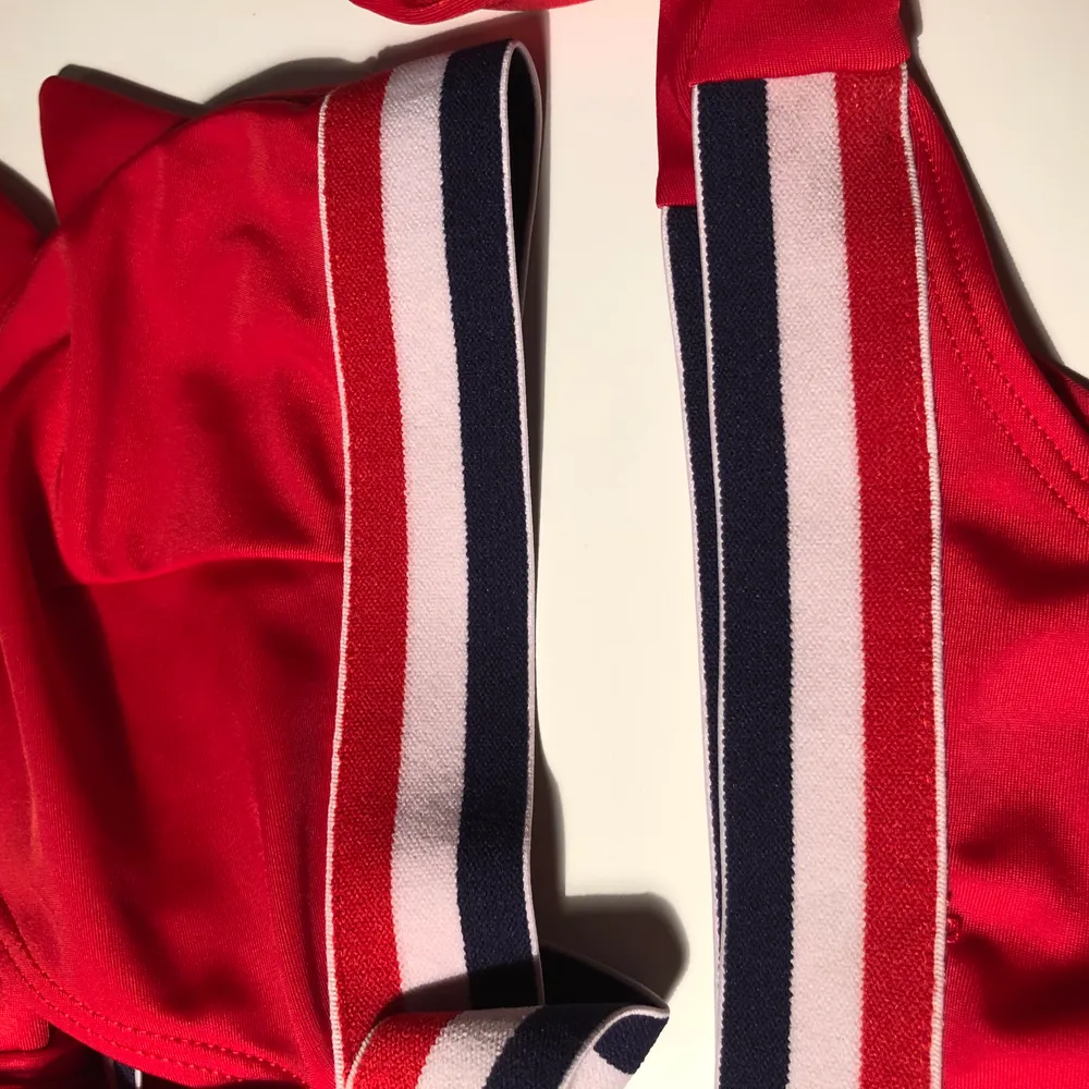 Röd bikini med blå och vita detaljer. Köptes inför en utlandsresa och använde en gång, därefter har den ej kommit till användning. . Övrigt.