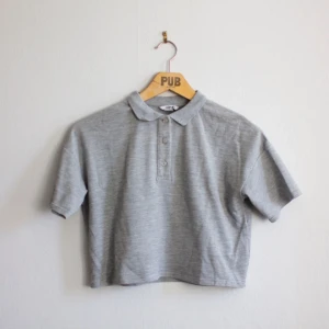  - Grå, croppad pikétröja från Monki. 