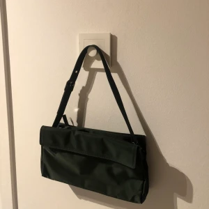 Grön baguettebag - Jättefin mörkgrön väska, väldigt praktisk. Rosa på insidan. Inga skador, aldrig använd men inga lappar kvar. 