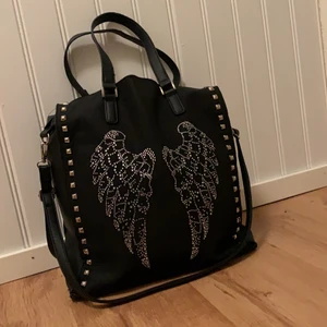 Väska  - Detta är en stor svart väska med ängel vingar på, den har används få gånger och är nästan helt oanvänd. Väskan har två mindre handtag och ett större. Det är helt svart inuti, och man får plats med mycket i. 