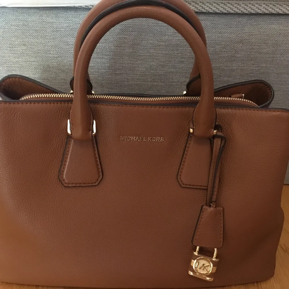 Ny MK väska med brun färg, som enkelt matchar kläder. Den har två stora fickor med magneter, en stor ficka med blixtlås och fem små fickor inuti. Bra för både avslappnad och arbete. Väskor.