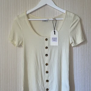 Topp med låg urringning och knappar - Ett Helt ny topp, kort armen med knappar i färg Cream *kan var lite tunna. Passa i alla vardagars outfit.
