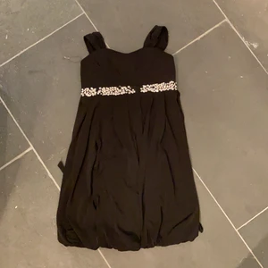 Svart klänning - Svart klänning i storlek 14 år (passar en ”kort” xs) lite glitter borta men ser mer ut som en detalj och inget trasigt! Snörning där bak så den sitter perfekt och som en fin detalj! 