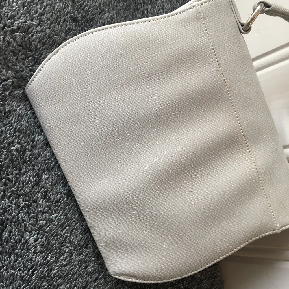 Oanvänd grå väska med tillhörande axelrem. Ny men har dock fått små vita fläckar på baksidan efter att ha lurat länge mot en vägg. . Väskor.