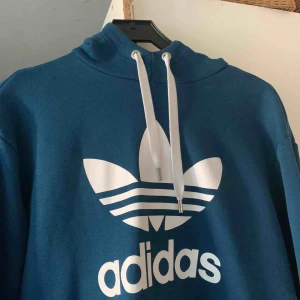  - Detta är en blå adidas hoodie som är blommig i luvan. Tröjan är använt bara 2 gånger och är i jätte bra skick. Den kostar 1100kr vanligtvis.