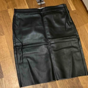  - Kjol i konstskinn i tight och figurnära modell med slits baktill. Aldrig använd, lapp kvar. 