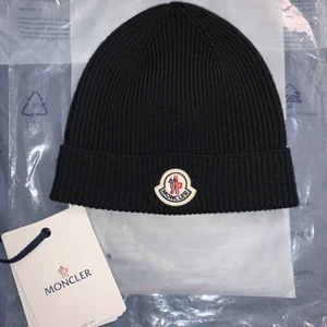 Moncler mössa  - Säljer en helt oanvänd moncler-mössa i one size. Passar både killar och tjejer.
