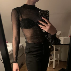 Glittrig tröja - Super fin svart glittrig topp från Gina Tricot. Använd 2-3 gånger men är i bra skick, säljs pga används ej. Har som en låg turtelneck och långa armar, passar strl XS