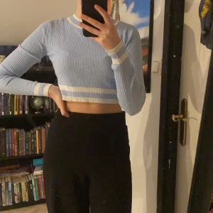 Ljusblå topp - En fin ljusblå topp med vita detaljer. Kort i midjan. Väldigt stretchigt material. Frakt tillkommer.