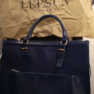  - En mörkblå praktisk väska med axelband till. Väskan är helt oanvänd, det finns 4 stora "fickor" och 3 små. Man får plats med väldigt mycket trots att den inte är jättestor. Kan skickas mot porto.