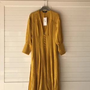  - Säljer en klänning i kimono-stil med slits i sidan, senapsgul och världens härligaste kvalité. Aldrig använd och lappen finns kvar! Storlek XS/S. Köparen betalar frakten.