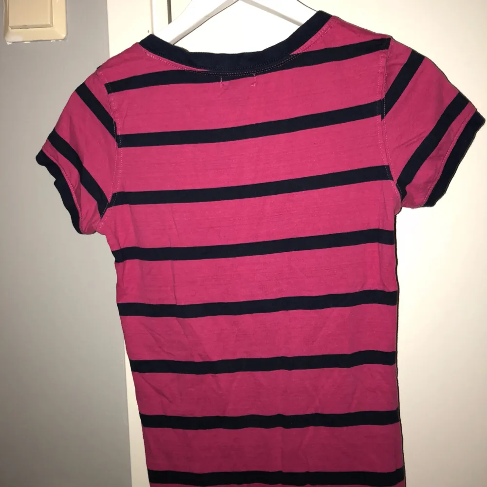Randig T-shirt från US POLO ASSN. Går i färgerna rosa med mörkblåa ränder. Använd fåtal gånger. Köparen står för frakten.. T-shirts.