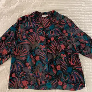 Färgglad mönstrad skjorta i 100 % polyester. Skönt silkesliknande material. Mönstrad i färgerna rosa, turkos, brun och svart. Har knappar och en krage.