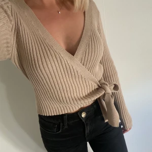 Stickad omlott tröja  - Beige tunnstickad tröja som man knyter omlott. Mycket bra skick. 170kr inklusive frakt.