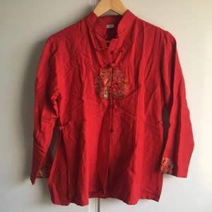 Röd asiatisk jacka/tröja med hög krage och fina knappar. Slits i sidorna och emblem på jackans ärmar och mage. Nyskick. 100% silke står det på lappen. Tar swish 🛵💨