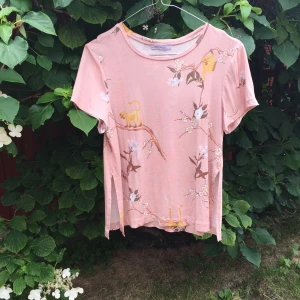  - T-shirt med blommönster och sprund, två små hål på axeln annars fin se en av bilderna. 